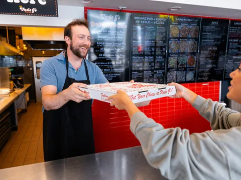 A pizza box being handed to a customer at the Uncle G's counter