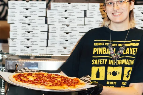 An Uncle G's crew member smiling in front of stacks of Uncle G's pizza boxes