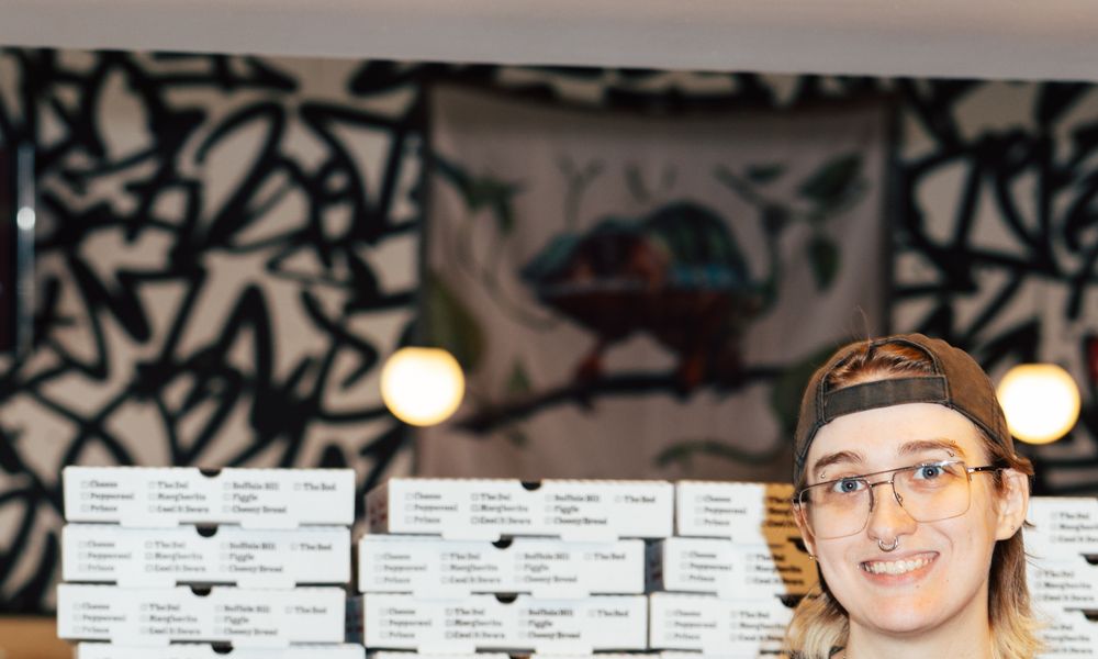 An Uncle G's crew member smiling in front of stacks of Uncle G's pizza boxes