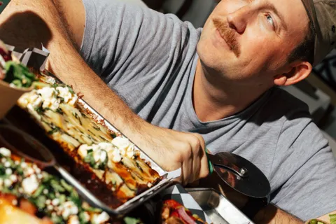 George cutting a Detroit-style pizza with a wheel, shot at a tilted angle