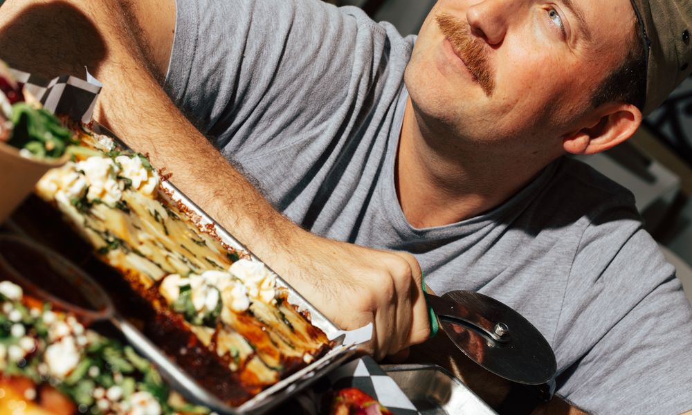 George cutting a Detroit-style pizza with a wheel, shot at a tilted angle