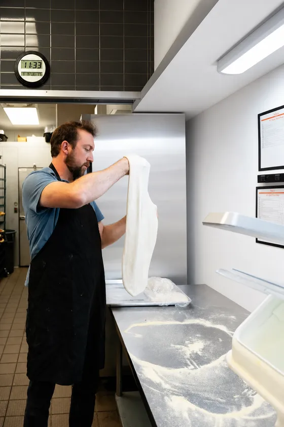George stretching pizza dough at a floured prep bench