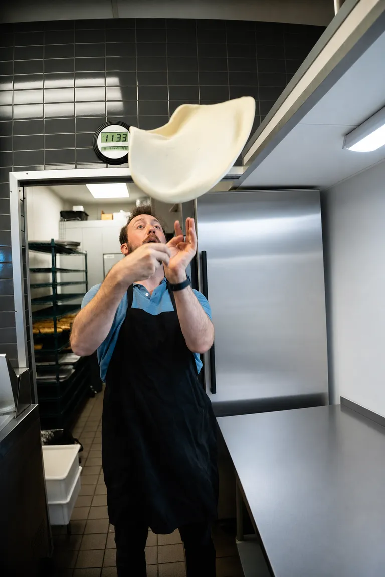 George tossing pizza dough in the air in the shop kitchen