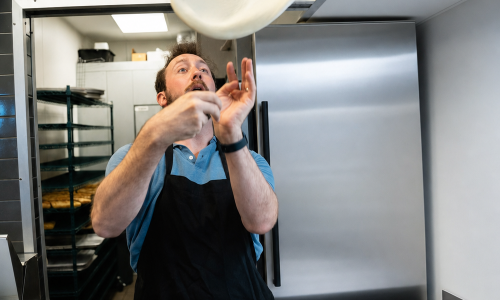 George tossing pizza dough in the air in the shop kitchen