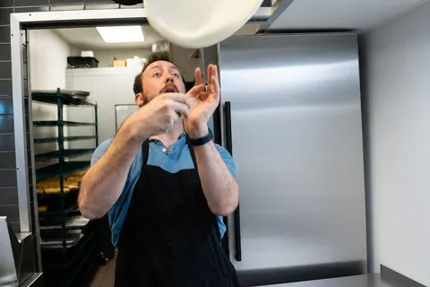 George tossing pizza dough in the air in the shop kitchen
