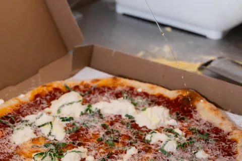 Drizzling hot honey over a boxed margherita pizza