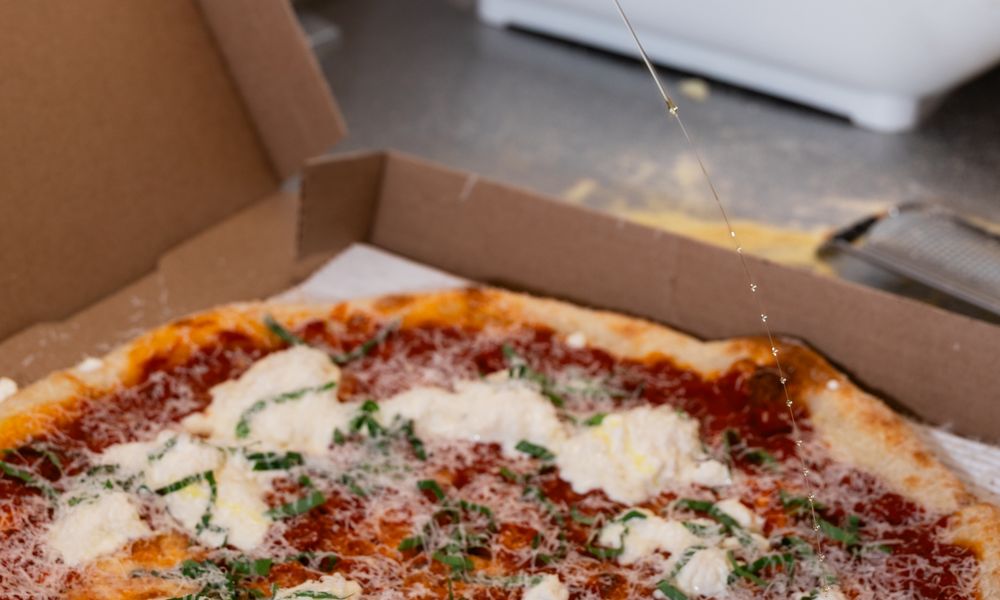Drizzling hot honey over a boxed margherita pizza