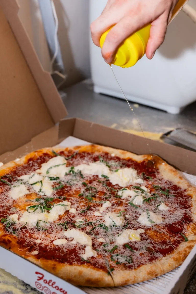 Drizzling hot honey over a boxed margherita pizza