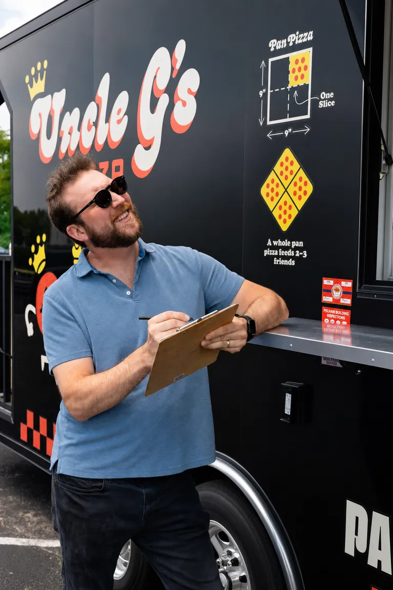 George taking notes on a clipboard in front of the Uncle G's trailer